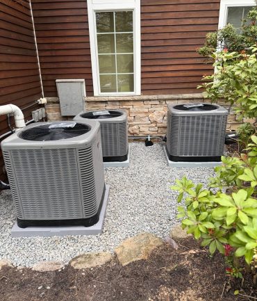 Three outdoor AC condenser units installed on a gravel pad against a wood-sided home by AFAB Construction